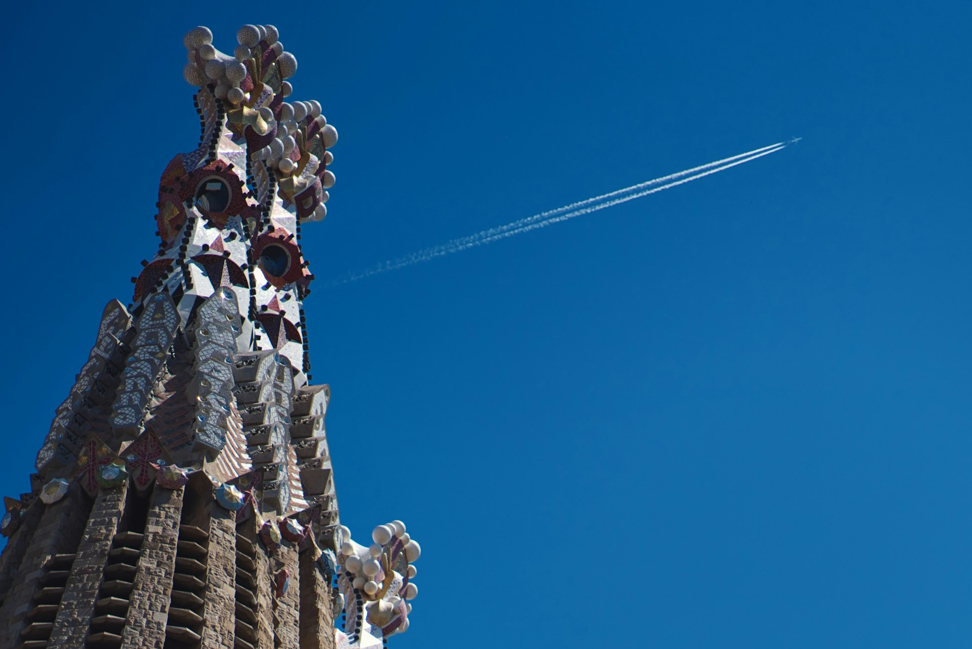 Airplane smoke trail above one of La Sagrada Familia’s towers.